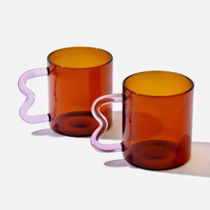 Amber glass mug with a pink wavy handle, modern handcrafted design