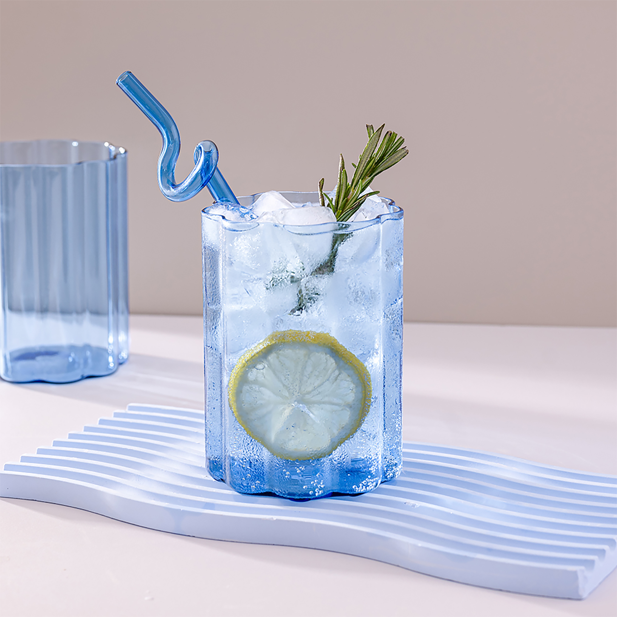 Refreshing lemon drink served in a Blue Ripple Glass with rosemary garnish and clear ice cubes.