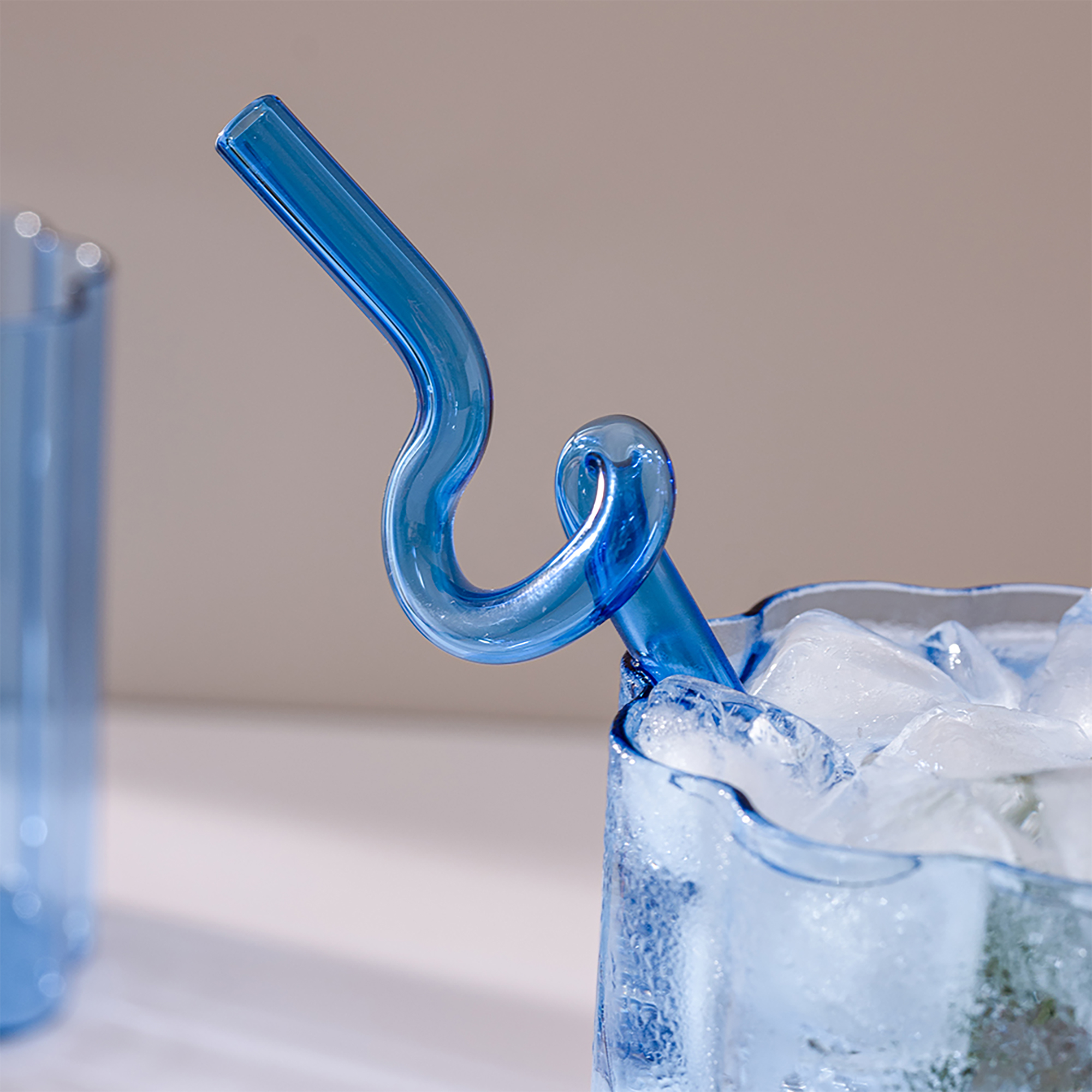 Blue glass sculpture with curling tubular shapes against a neutral background, abstract art.