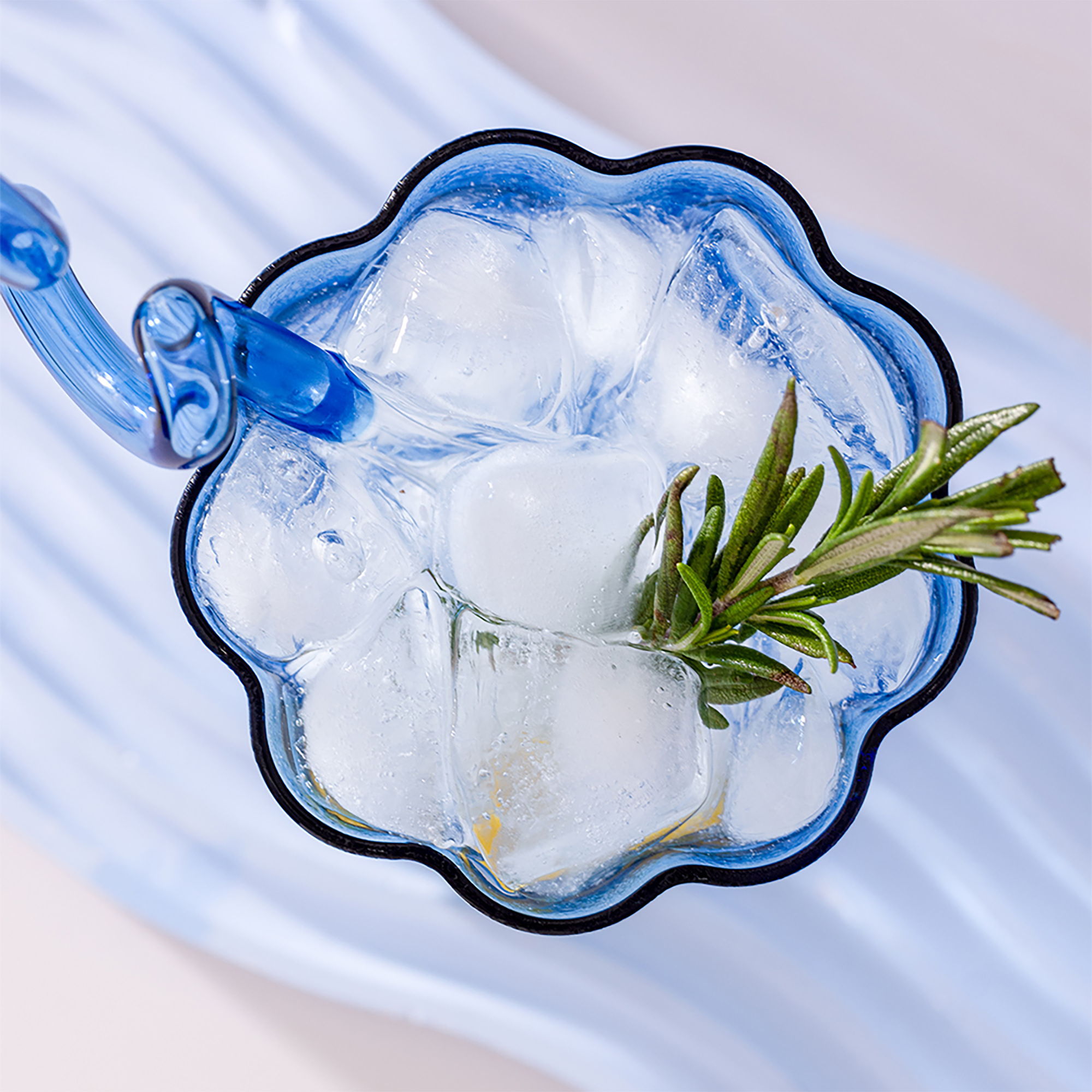 Top view of a Blue Ripple Glass filled with sparkling water, ice and fresh rosemary.